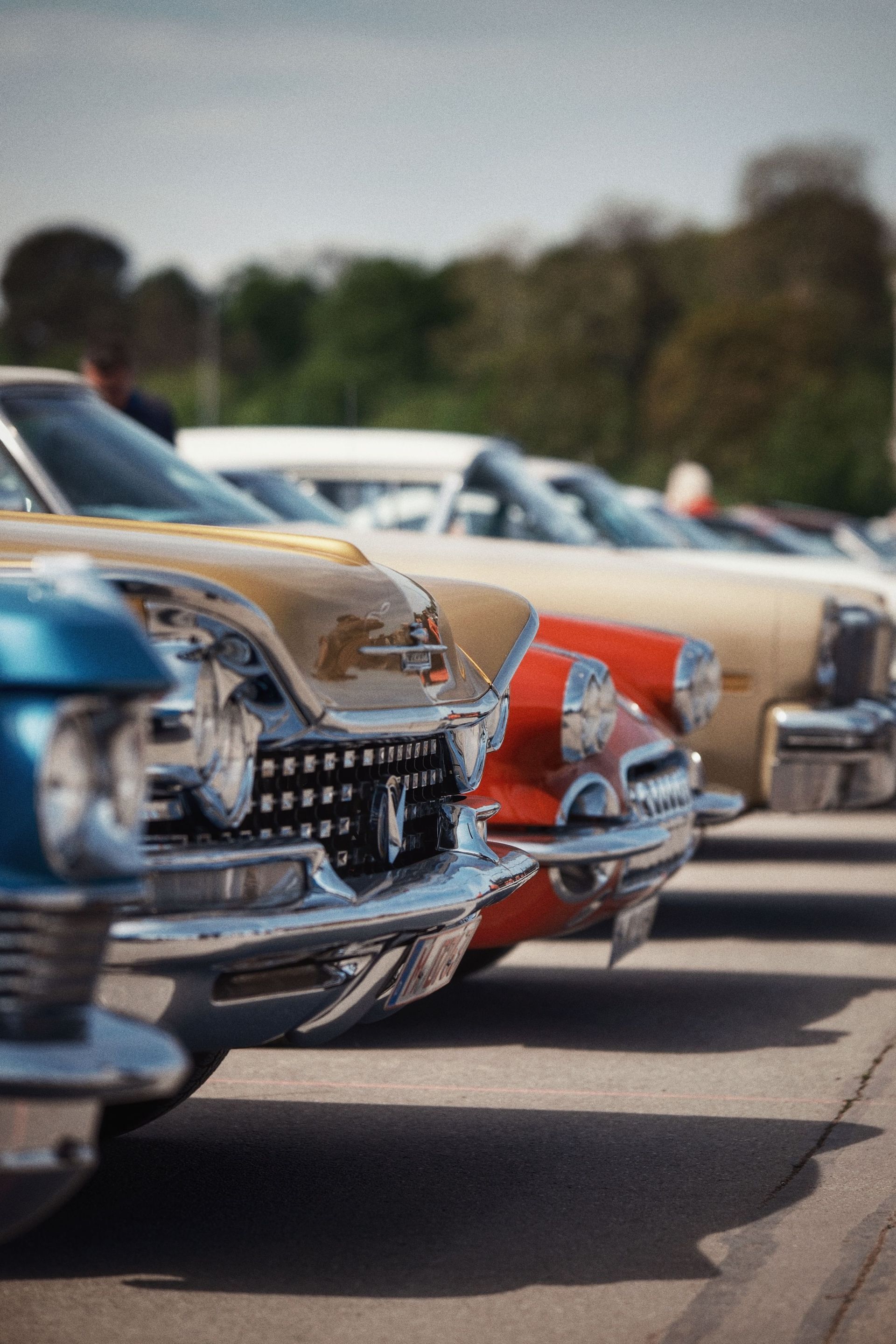 Row of classic cars parked outdoors, with a blue, orange, and beige car in the foreground