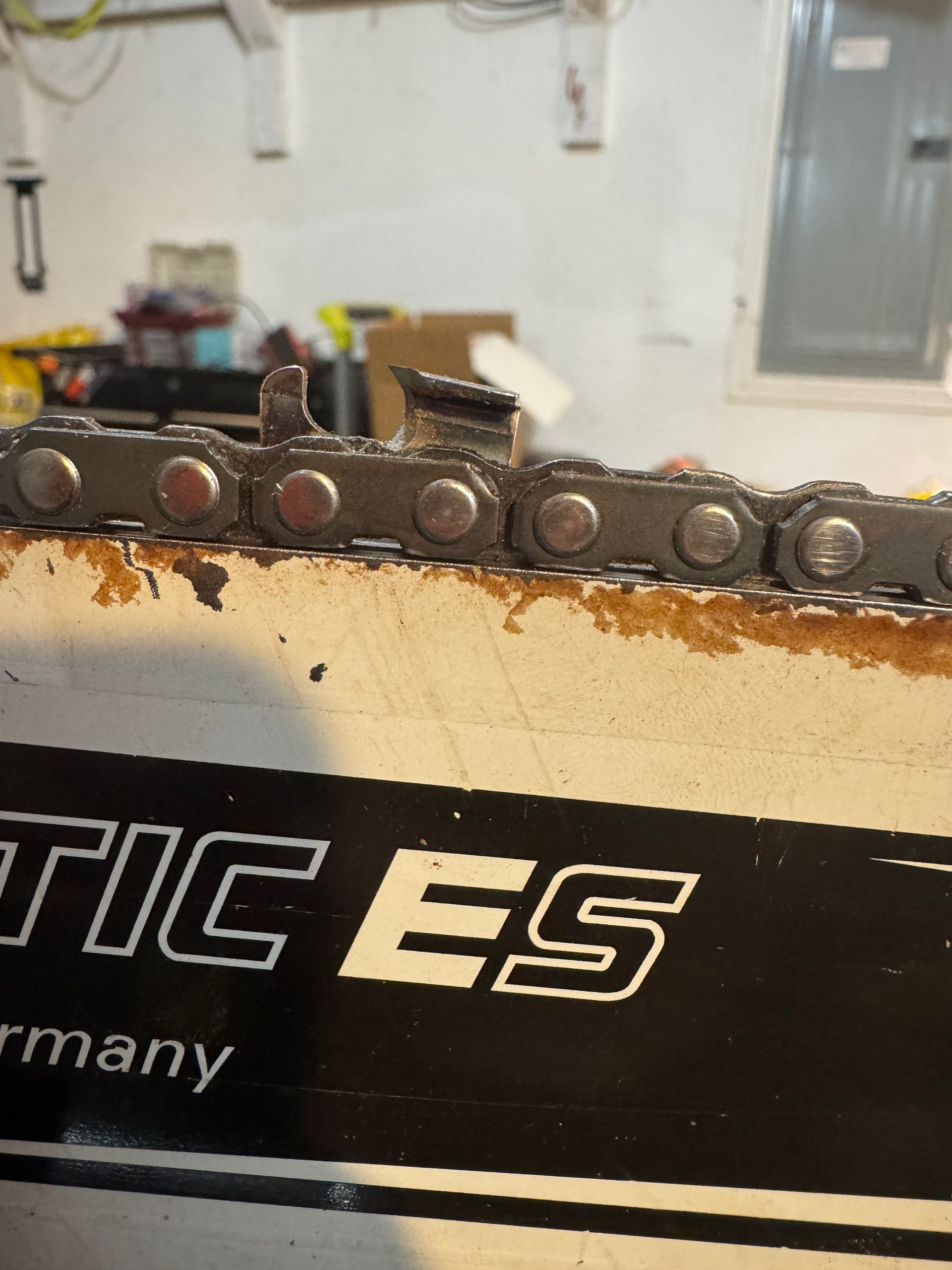 A close-up view of a chainsaw chain resting on its bar, showing a damaged cutter link that is bent upward.