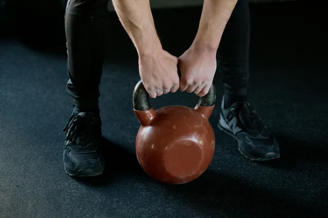 Hands lifting a brown 32 kg kettlebell on a gym floor