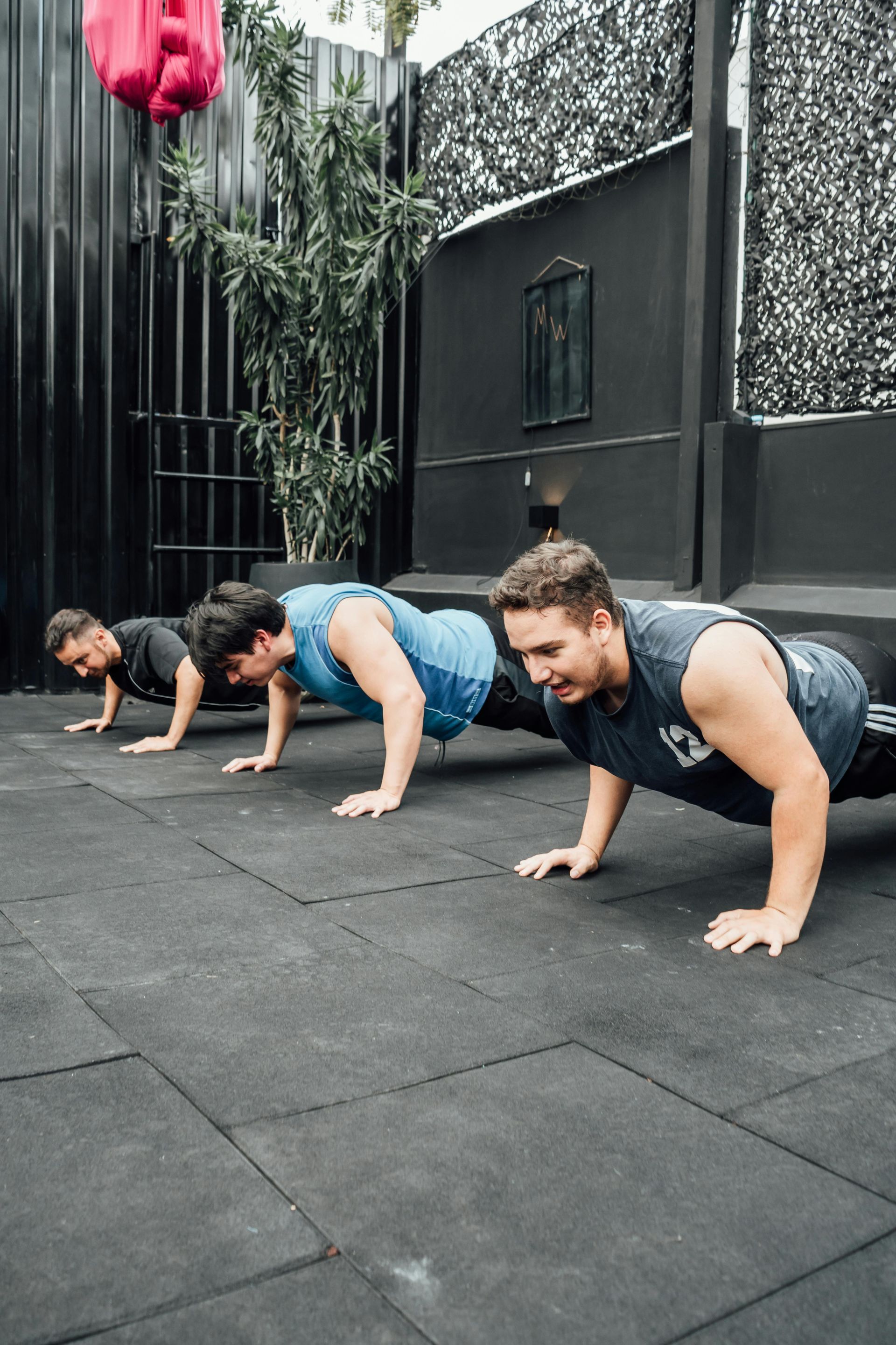 People doing push-ups on black mats outdoors in a fenced courtyard
