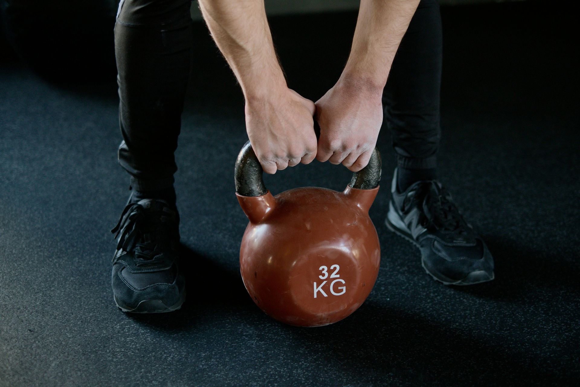 Hands lifting a brown 32 kg kettlebell on a gym floor