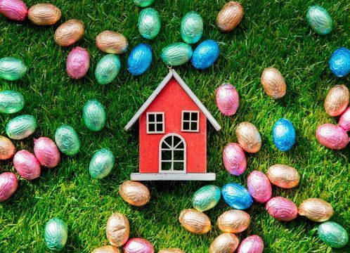Red toy house surrounded by colorful foil-wrapped Easter eggs scattered on green grass.
