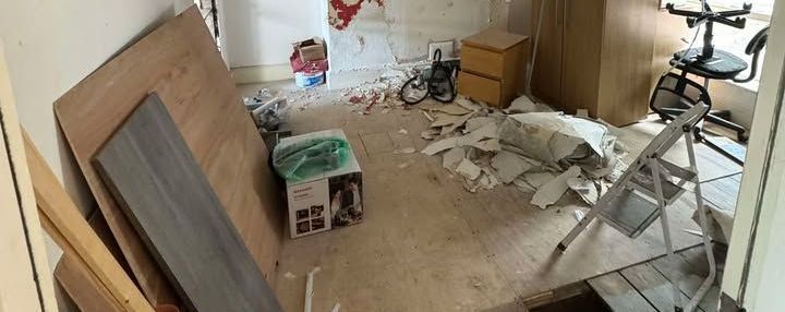 Room under renovation with debris on the floor, boards, and a step ladder.