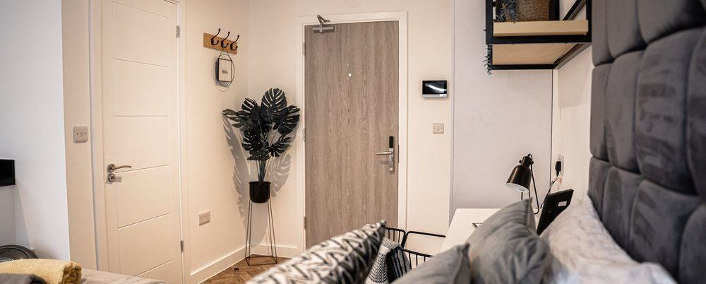 A bedroom with doors, a plant, and a bed with a gray headboard.