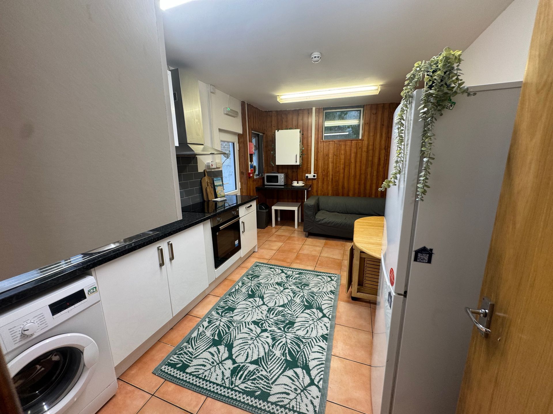 Kitchen with white cabinets, a black countertop, and a washing machine. A green rug lies on a tiled floor.