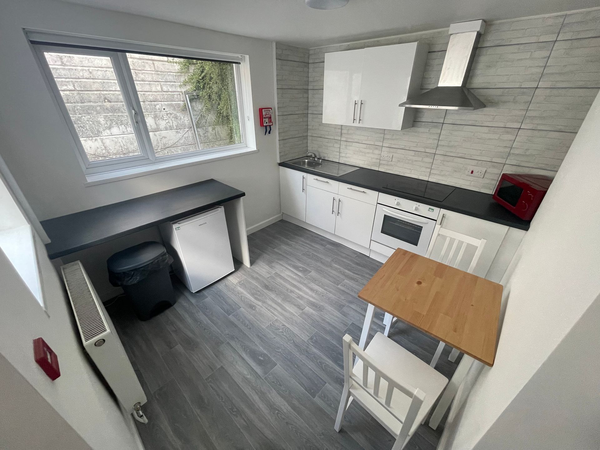 Small, modern kitchen with white cabinets, wooden table and chairs, a window, and a black counter.