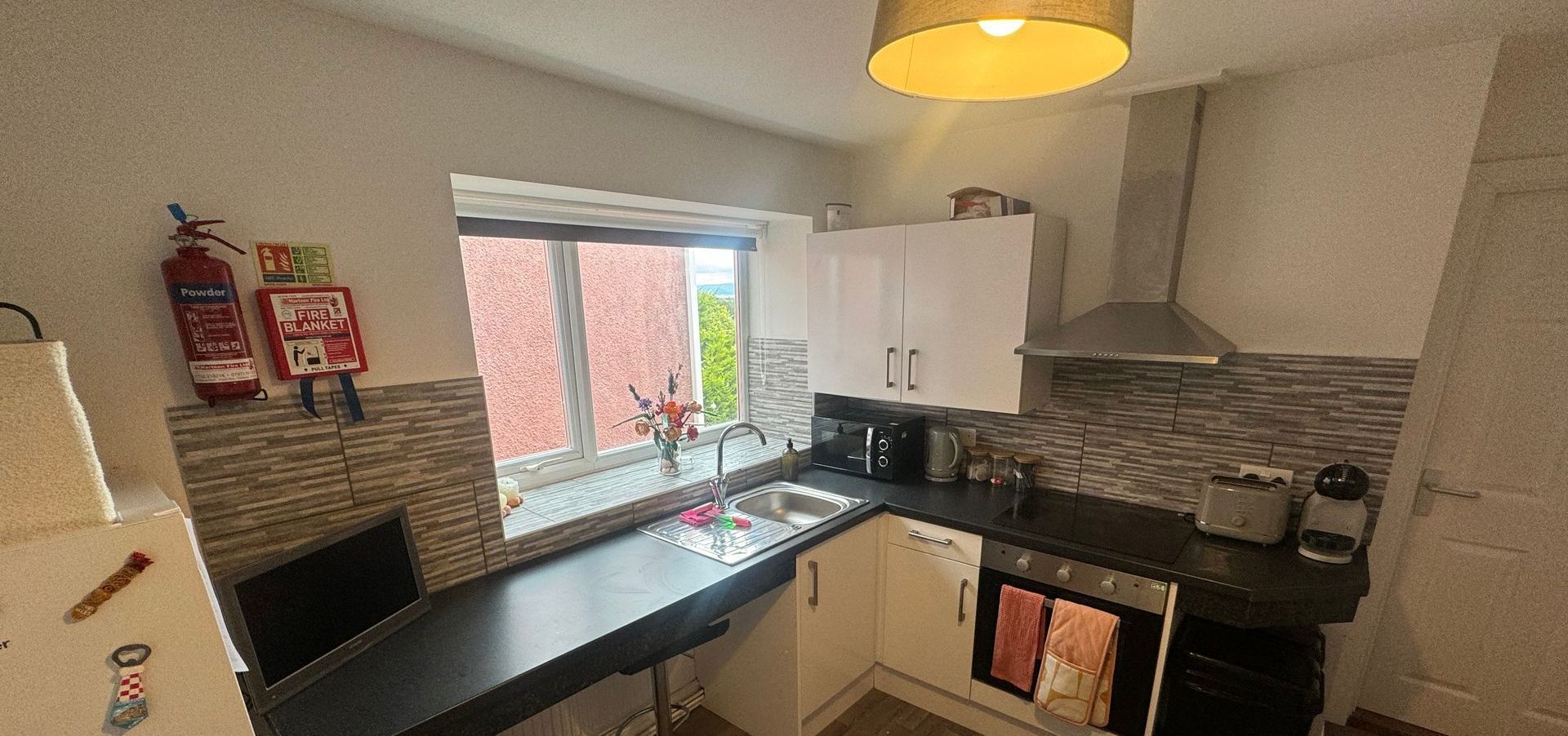 Kitchen interior with cabinets, window, oven, and a fire extinguisher on the wall.
