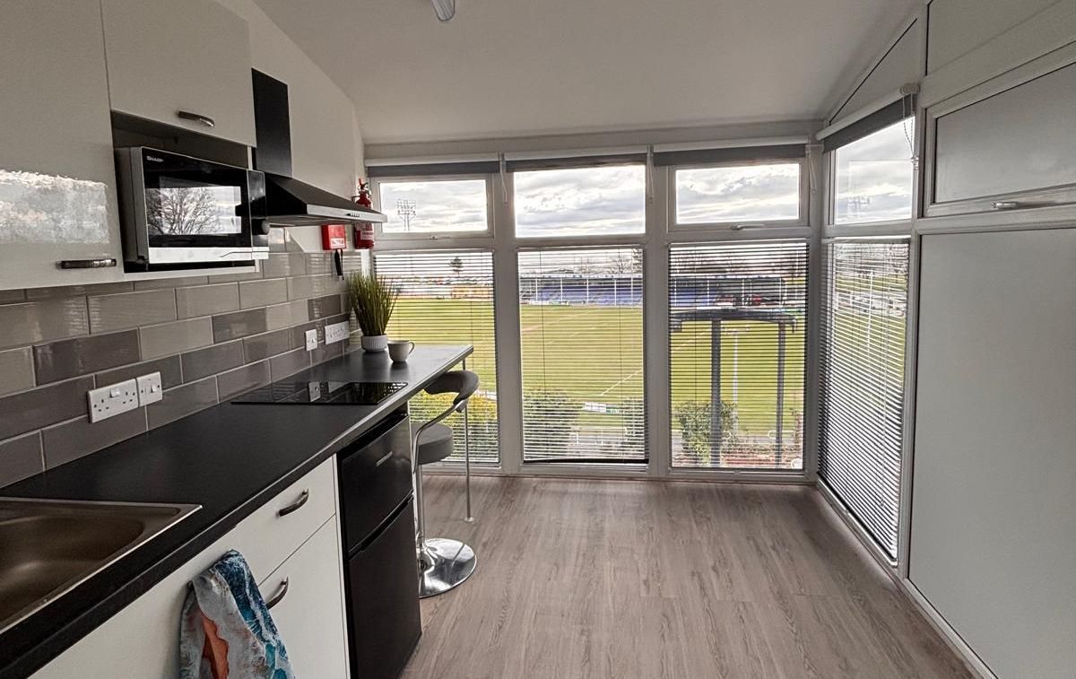 Modern kitchen with black countertops, oven, and large windows overlooking a grassy area.