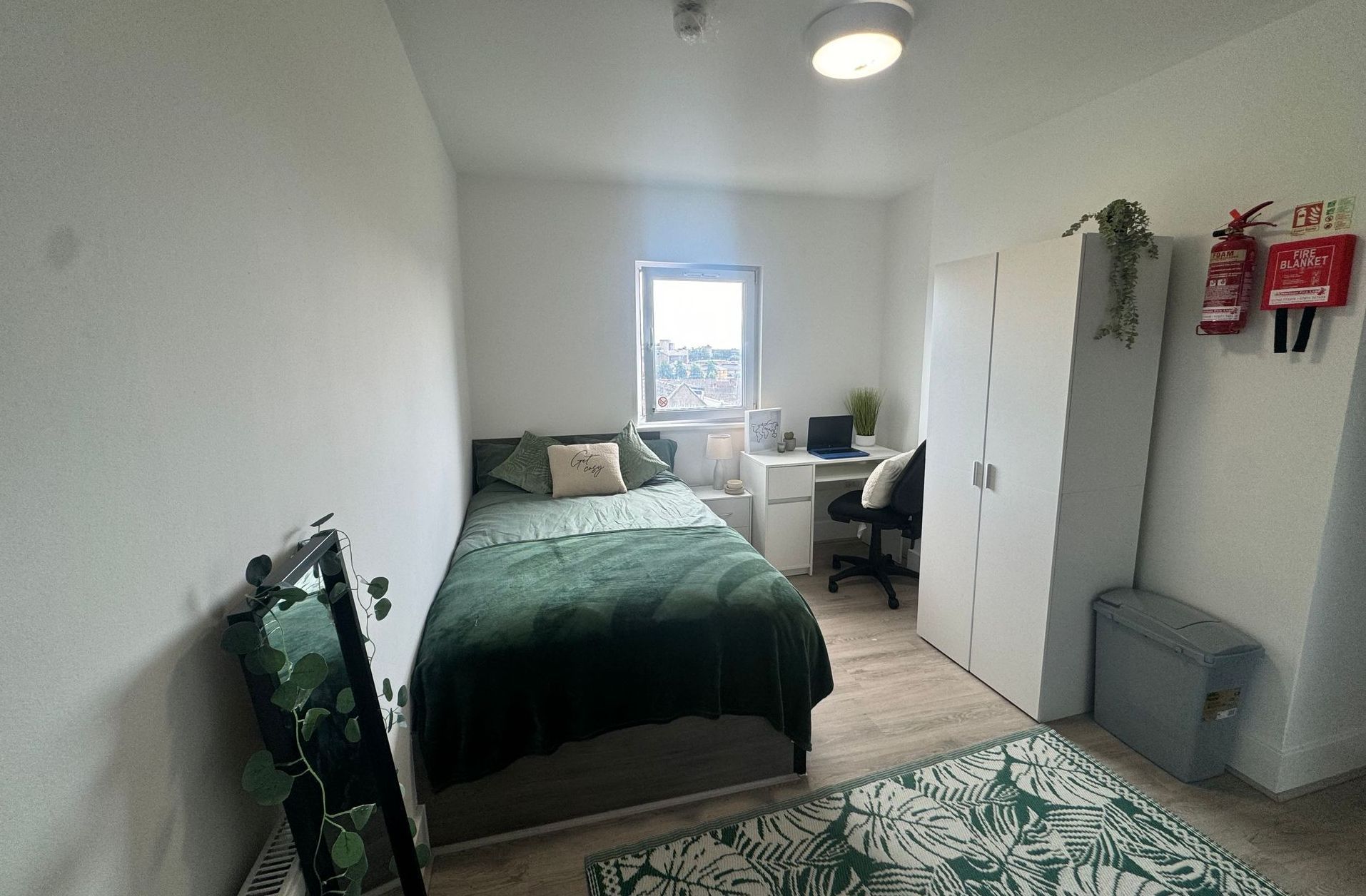 Small bedroom with a single bed, desk, wardrobe, and patterned rug.
