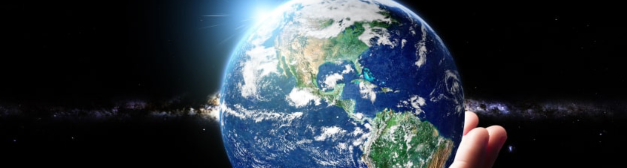 Hand holding Earth in space; blue oceans, green land, sunlight, dark background.