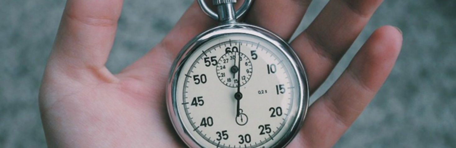 A hand holding a silver stopwatch. The time is just over 30 seconds.