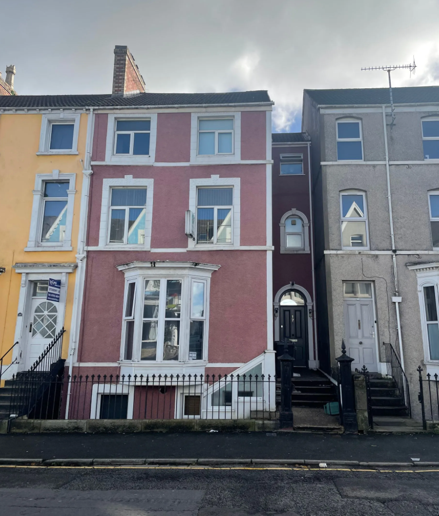 Row of colorful terraced houses on a street. The middle one is pink with a bay window.