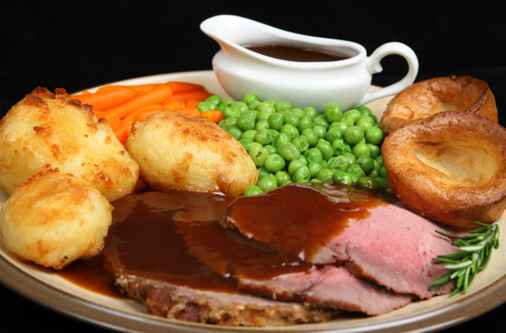 Roast beef dinner with gravy, potatoes, carrots, peas, and Yorkshire pudding.
