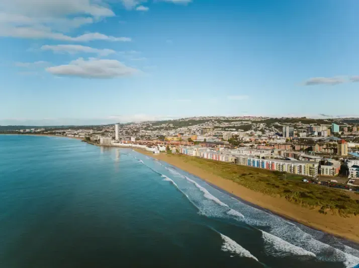Coastal cityscape with beach, buildings, and sea under a blue sky.
