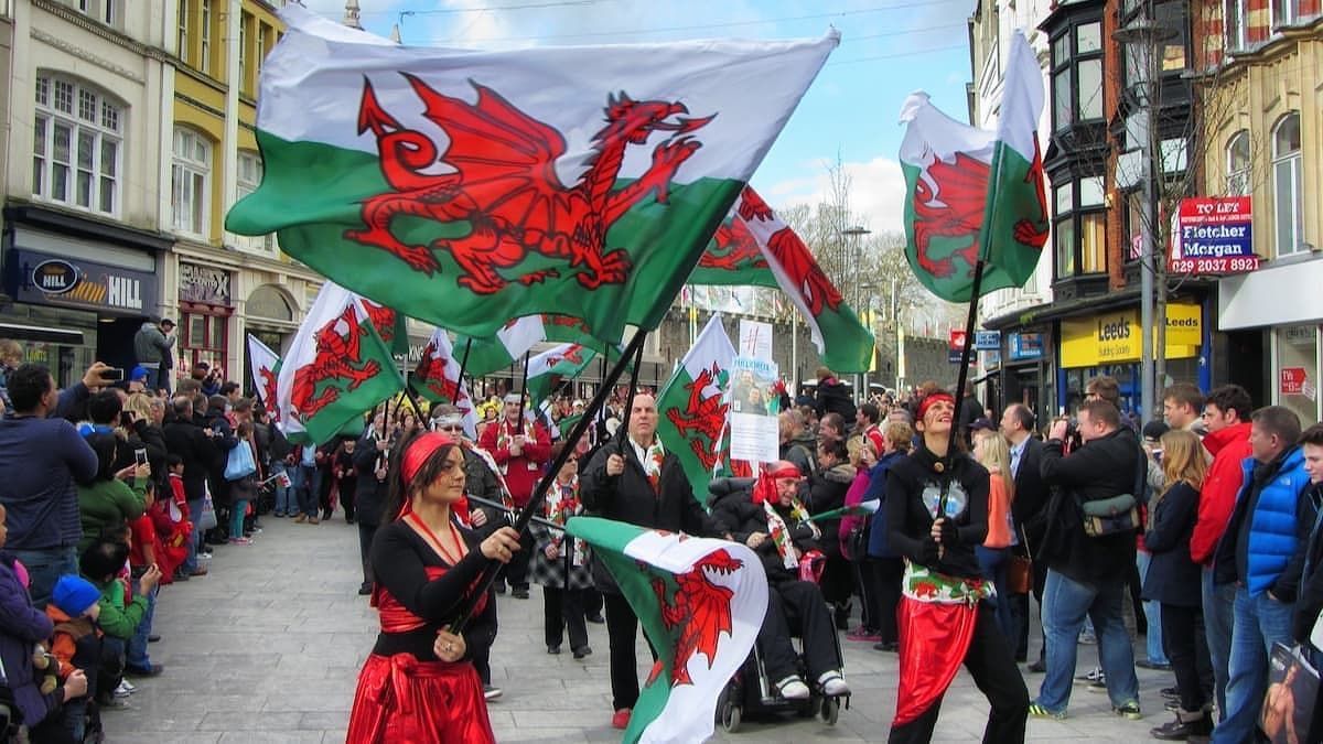 People waving Welsh flags in a street parade. The dragon flag is prominently displayed; red, green, and white colors.