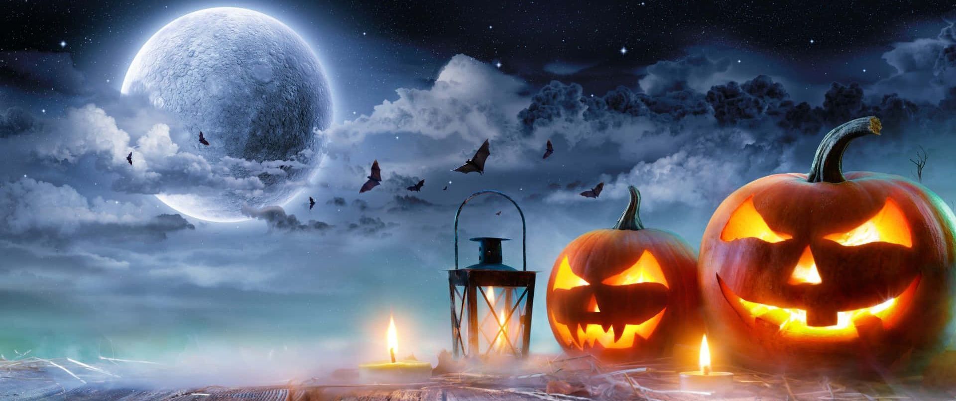 Two glowing jack-o'-lanterns, lantern, candles, bats, and full moon against a spooky night sky.