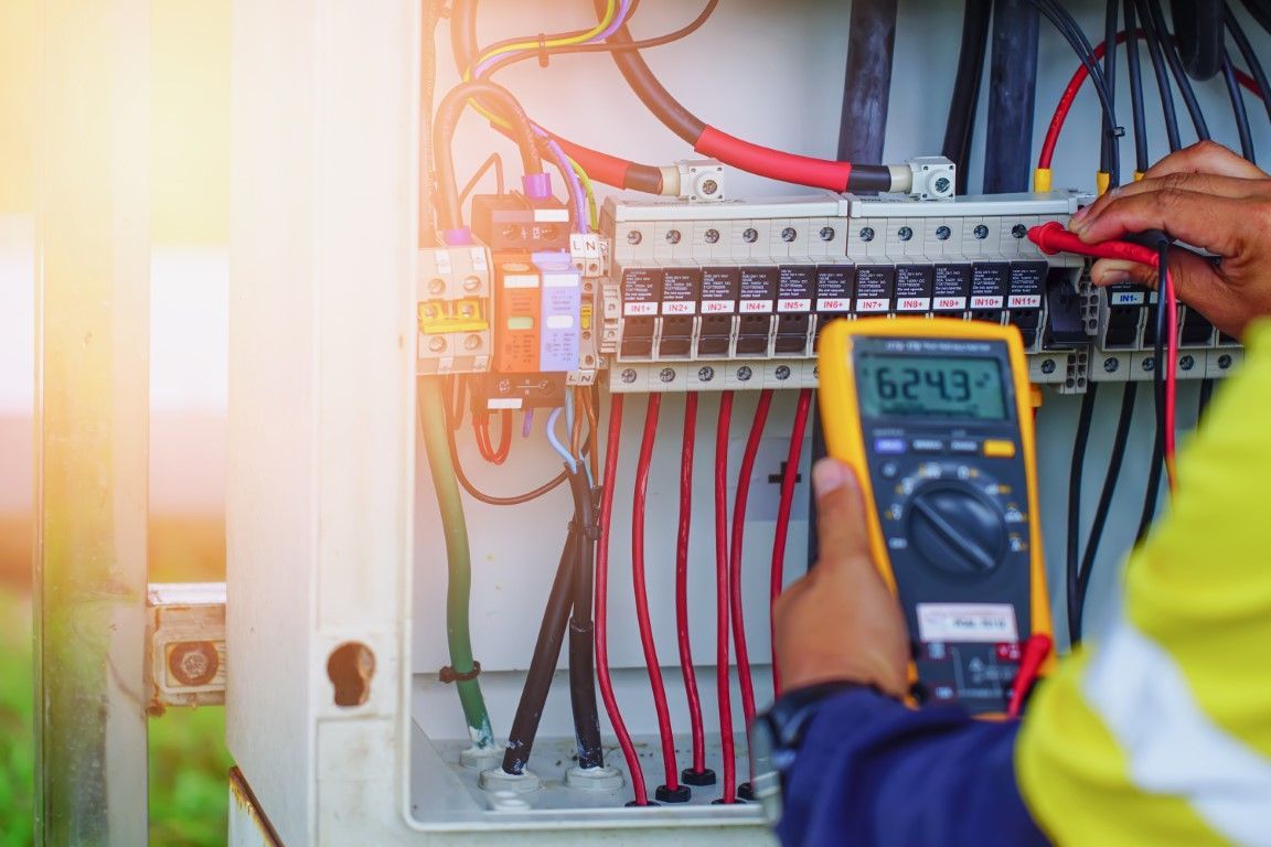 Electrician testing wiring in an open electrical panel with a digital multimeter