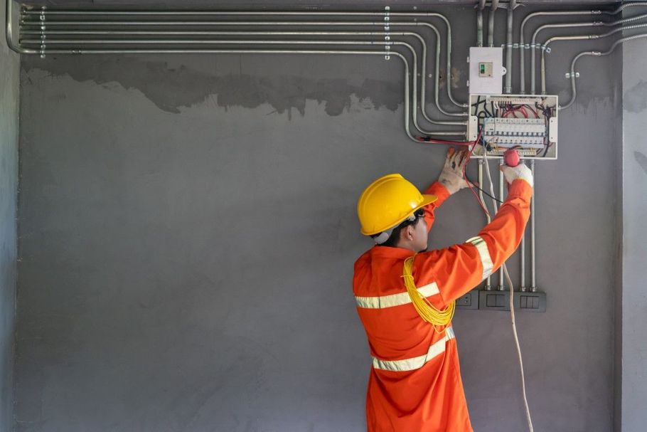 Worker in orange safety gear installing electrical conduit on a gray wall