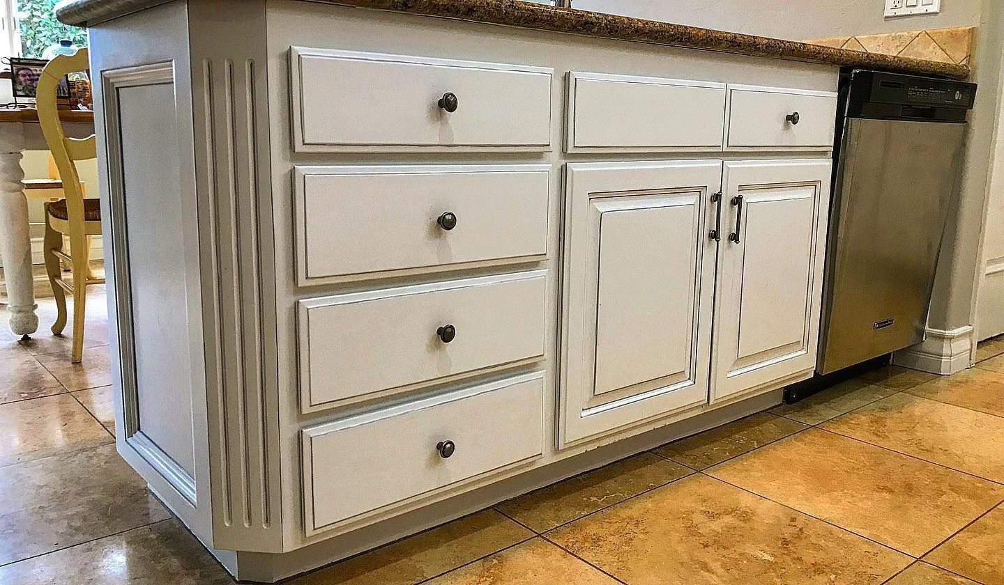 White kitchen island with drawers and cabinets, granite countertop, stainless steel dishwasher.