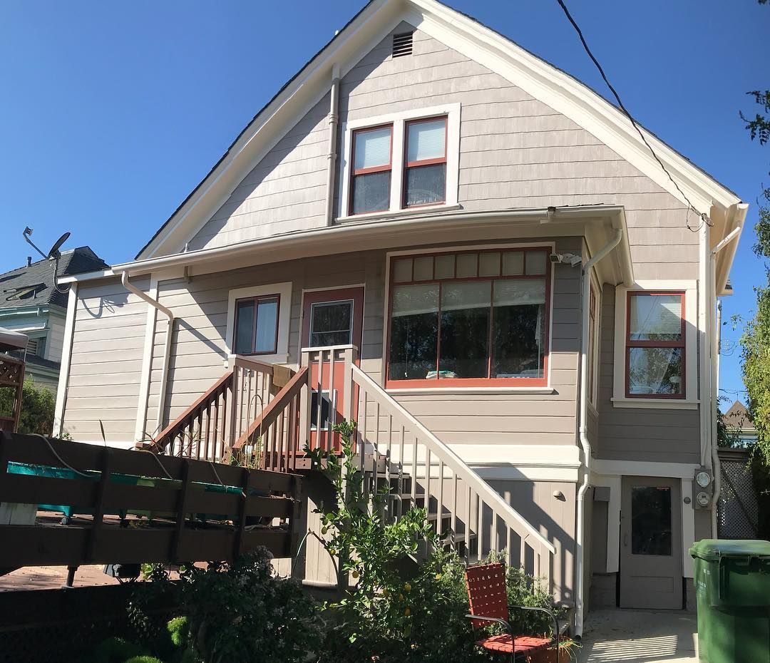 Two-story house with exterior stairs leading to a doorway. Light grey siding and white trim under a blue sky.