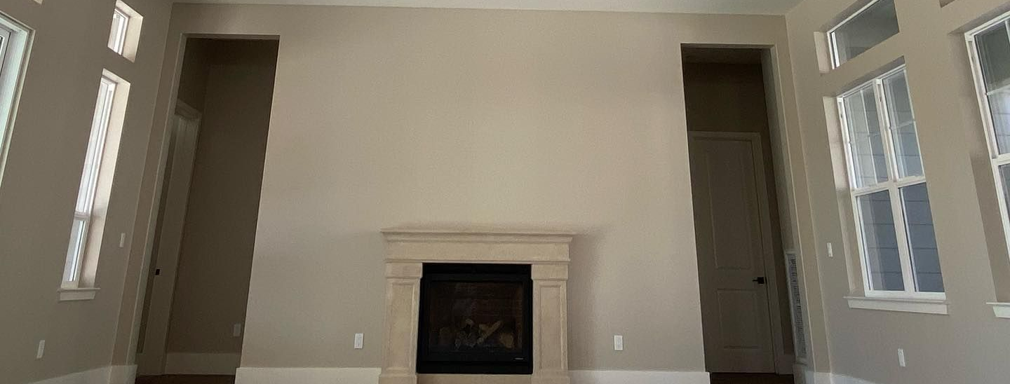 Living room with wood-paneled ceiling, beams, fireplace, and windows. Walls are beige.