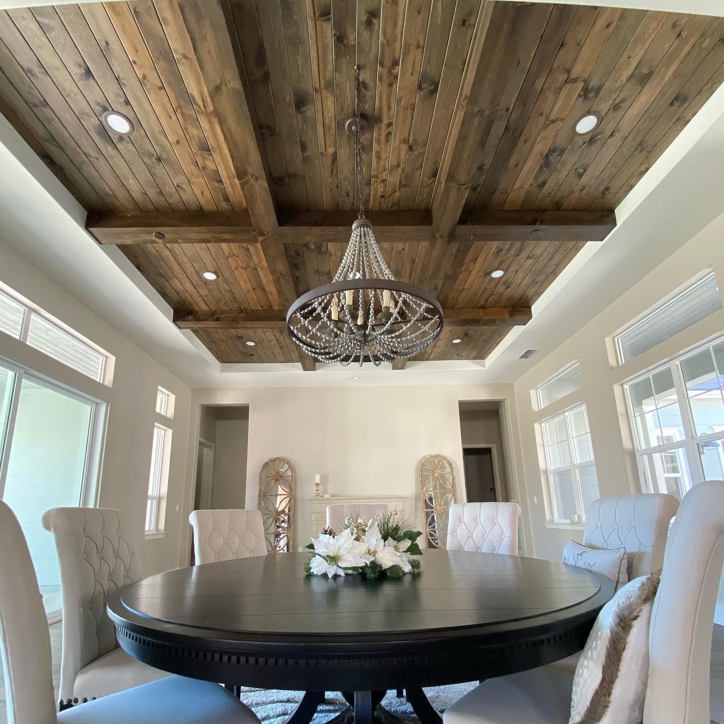 Dining room with dark wood ceiling beams, chandelier, round table, and upholstered chairs.