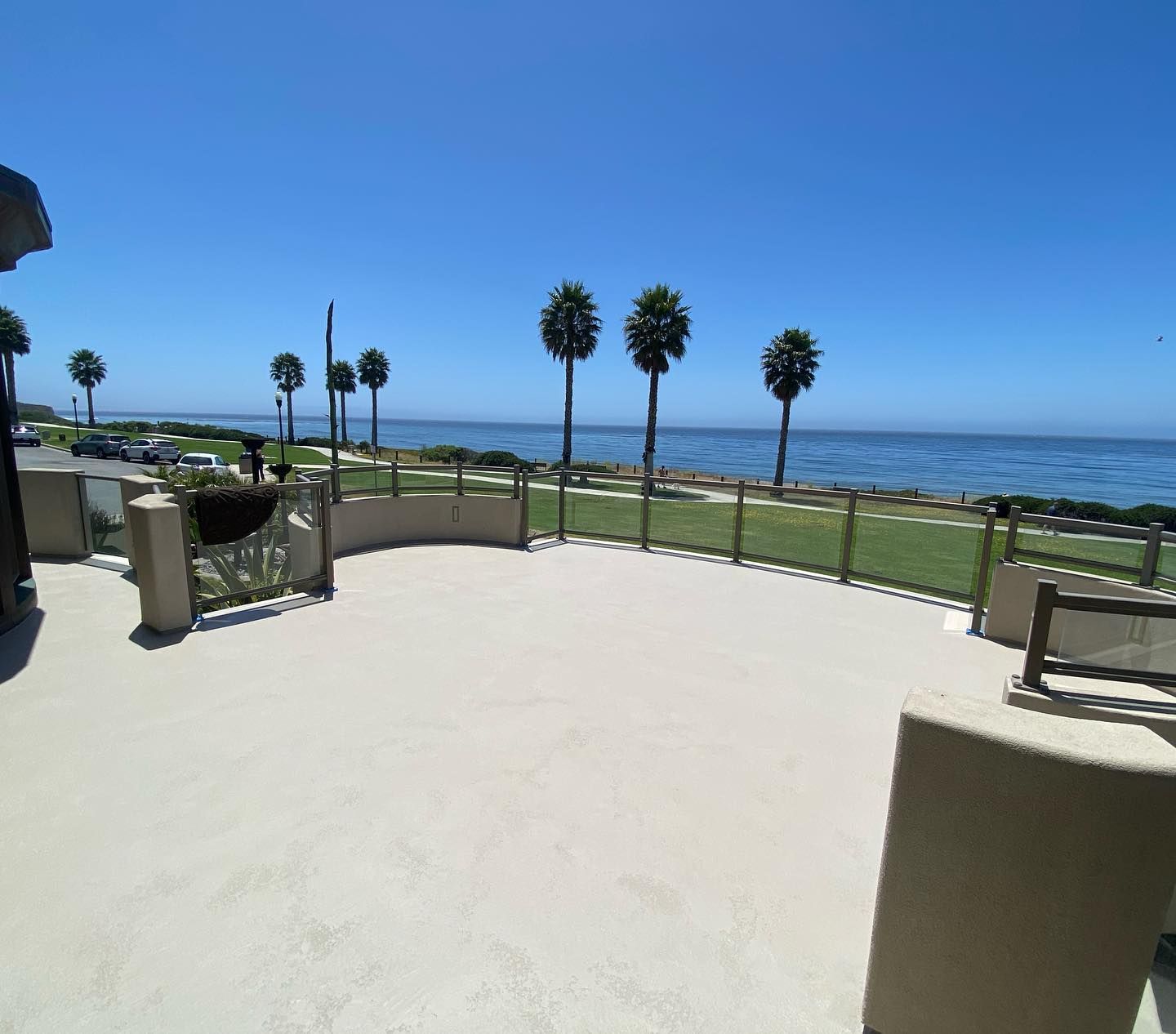 Exterior patio overlooking ocean with palm trees under a blue sky.