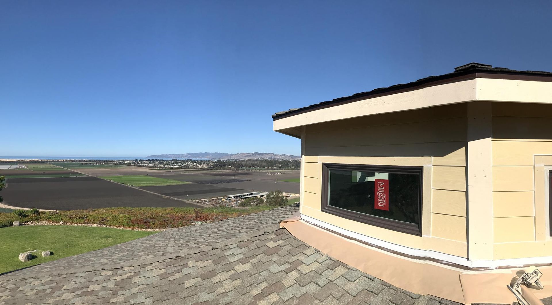 View from rooftop with cityscape, farmland, and clear blue sky. Beige building with window.