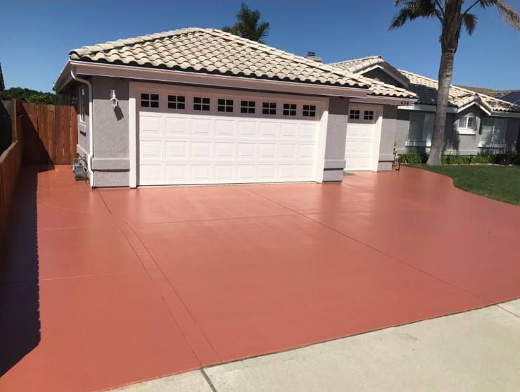 Red painted concrete driveway leading to a house with a white garage door.