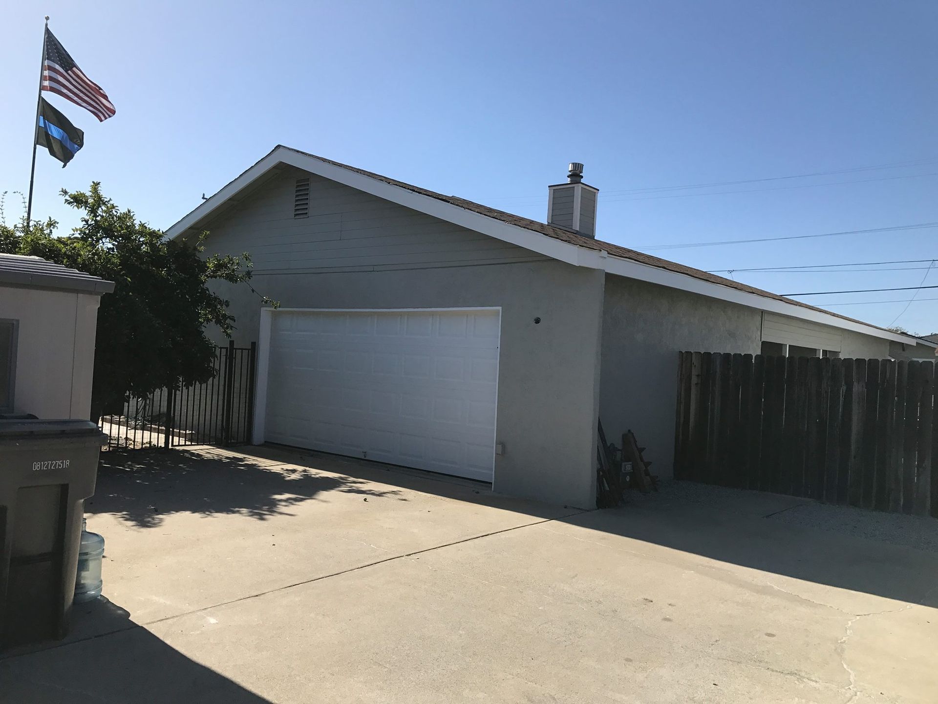 Exterior view of a house with a white garage door, concrete driveway, and American flag on a sunny day.