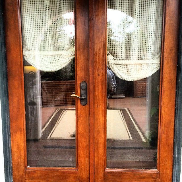 Wooden double doors with glass panels and a curtain, reflecting interior.