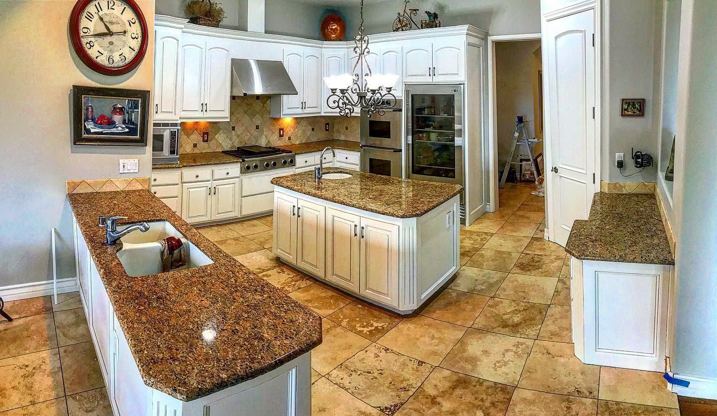 A large white kitchen with granite countertops, stainless steel appliances, and a central island.