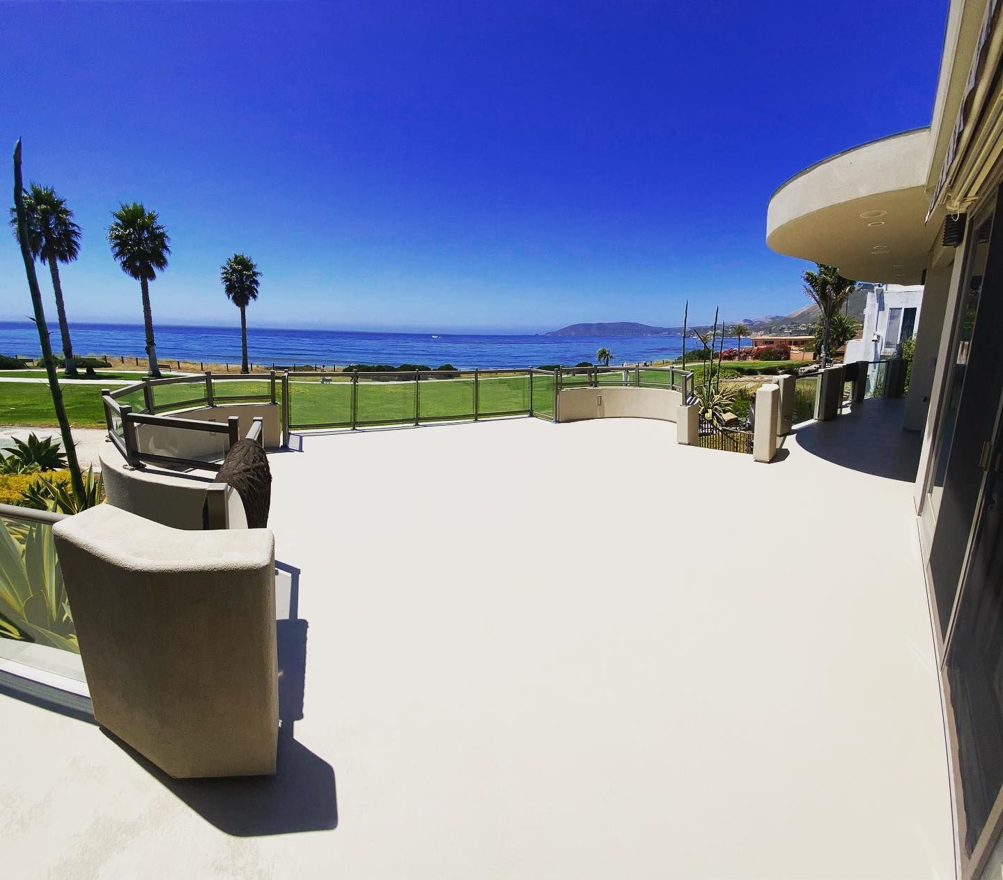 Patio overlooking ocean, with palm trees, blue sky, and white concrete.