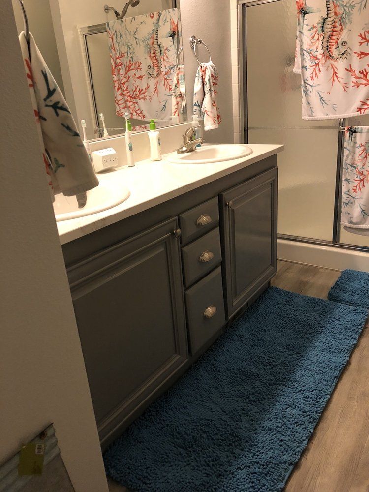 Bathroom with gray vanity, two sinks, blue rug, coral and white shower curtain.