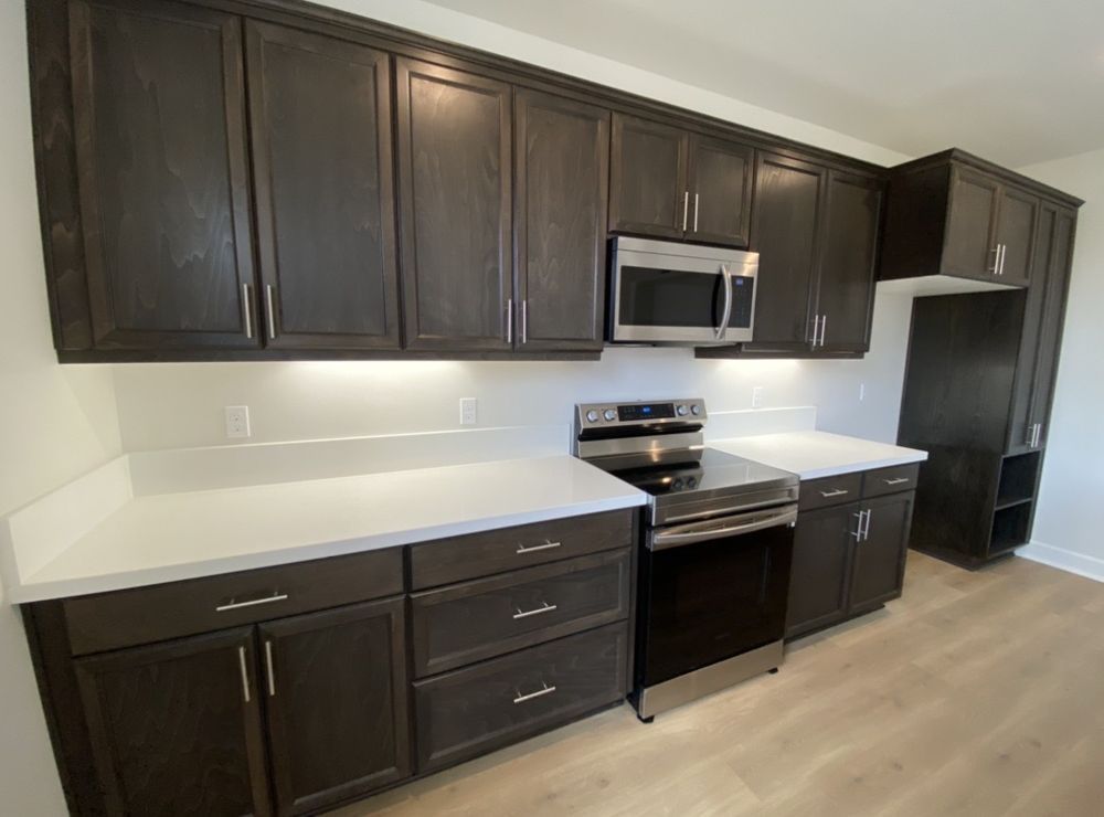 Dark wood kitchen cabinets with white countertops and stainless steel appliances.