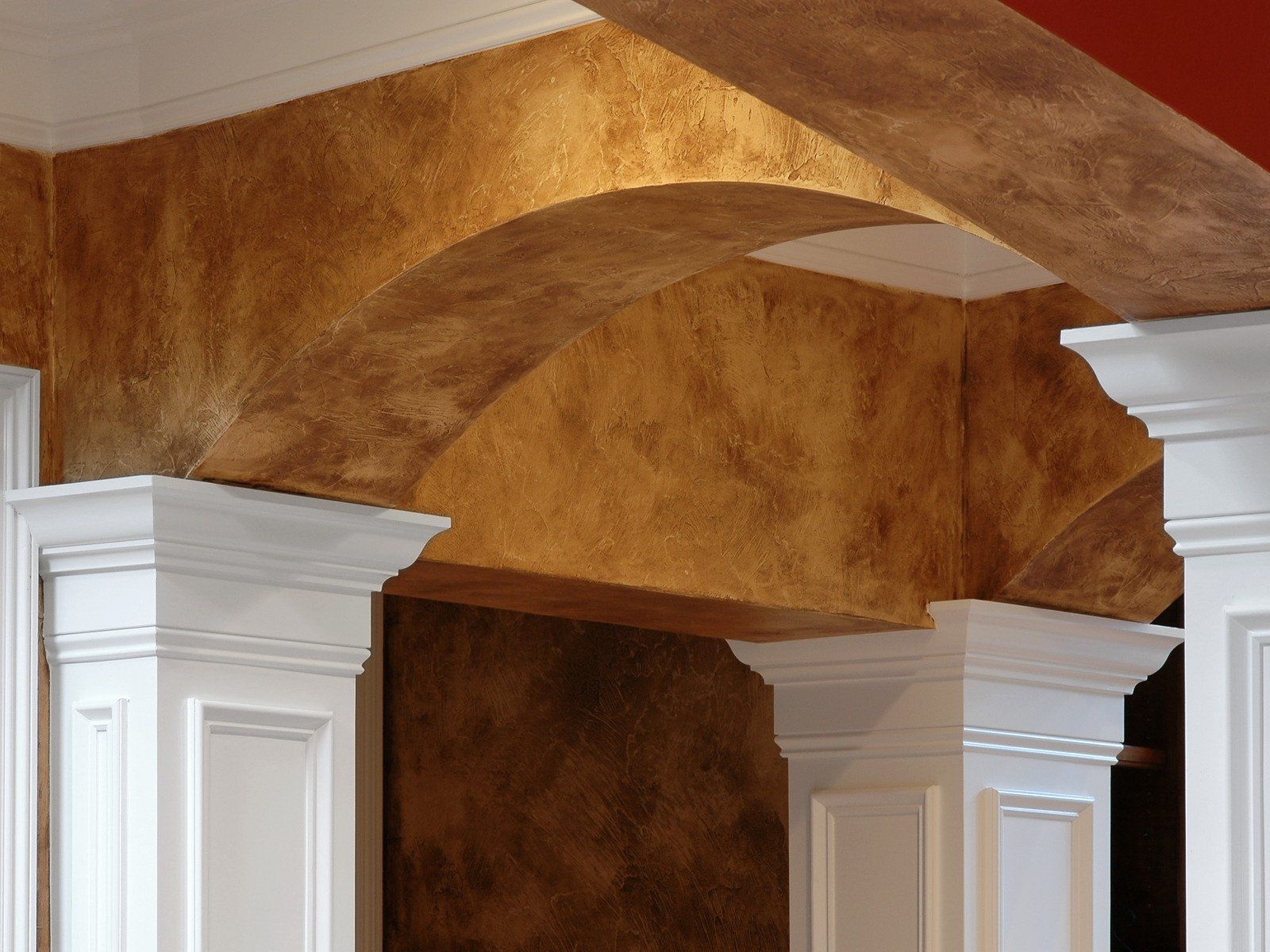 Ornate ceiling with arched detail, finished in textured brown and gold tones, supported by white pillars.