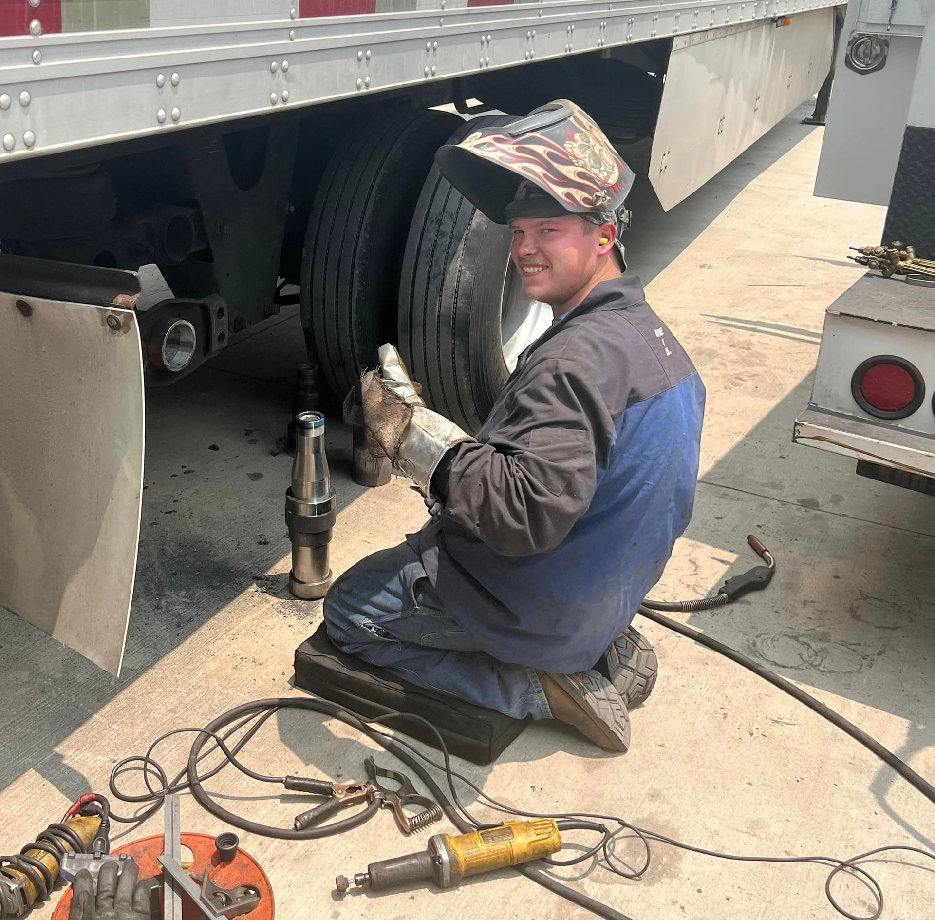 A man wearing a welding mask is working on a truck tire