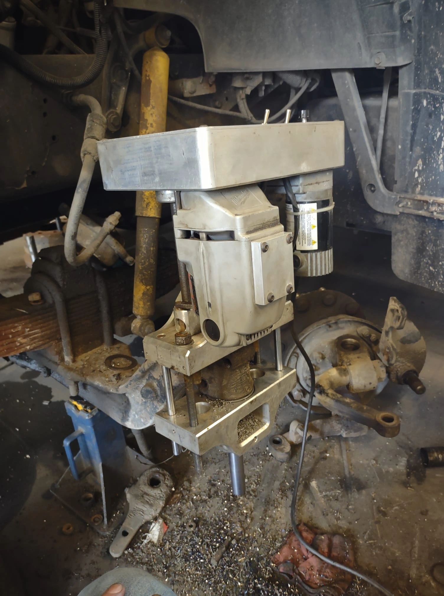 A drill is sitting underneath a car in a garage.