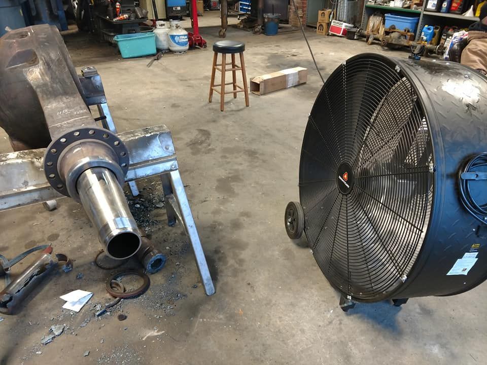 A large fan is sitting next to a pipe in a garage