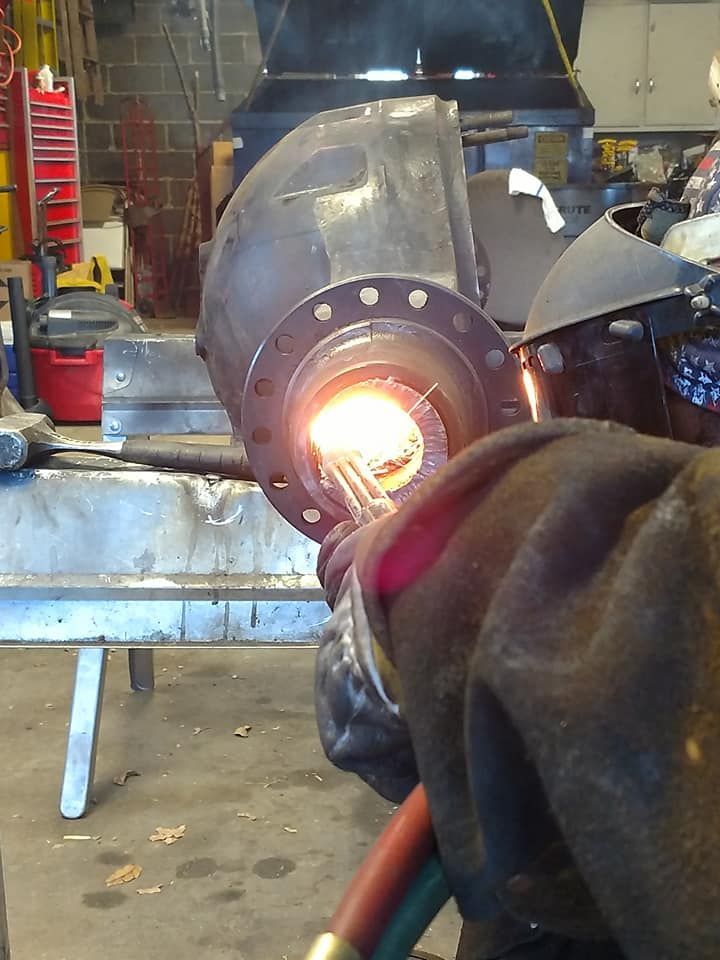 A man wearing a welding helmet is welding a piece of metal
