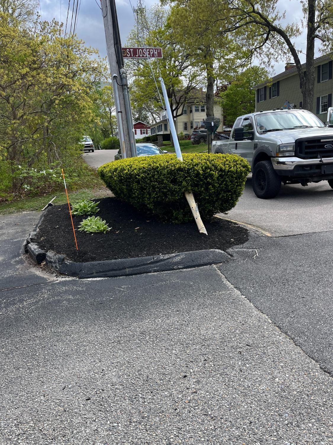 Corner planting bed with a trimmed bush, street sign, and a truck parked on the street.