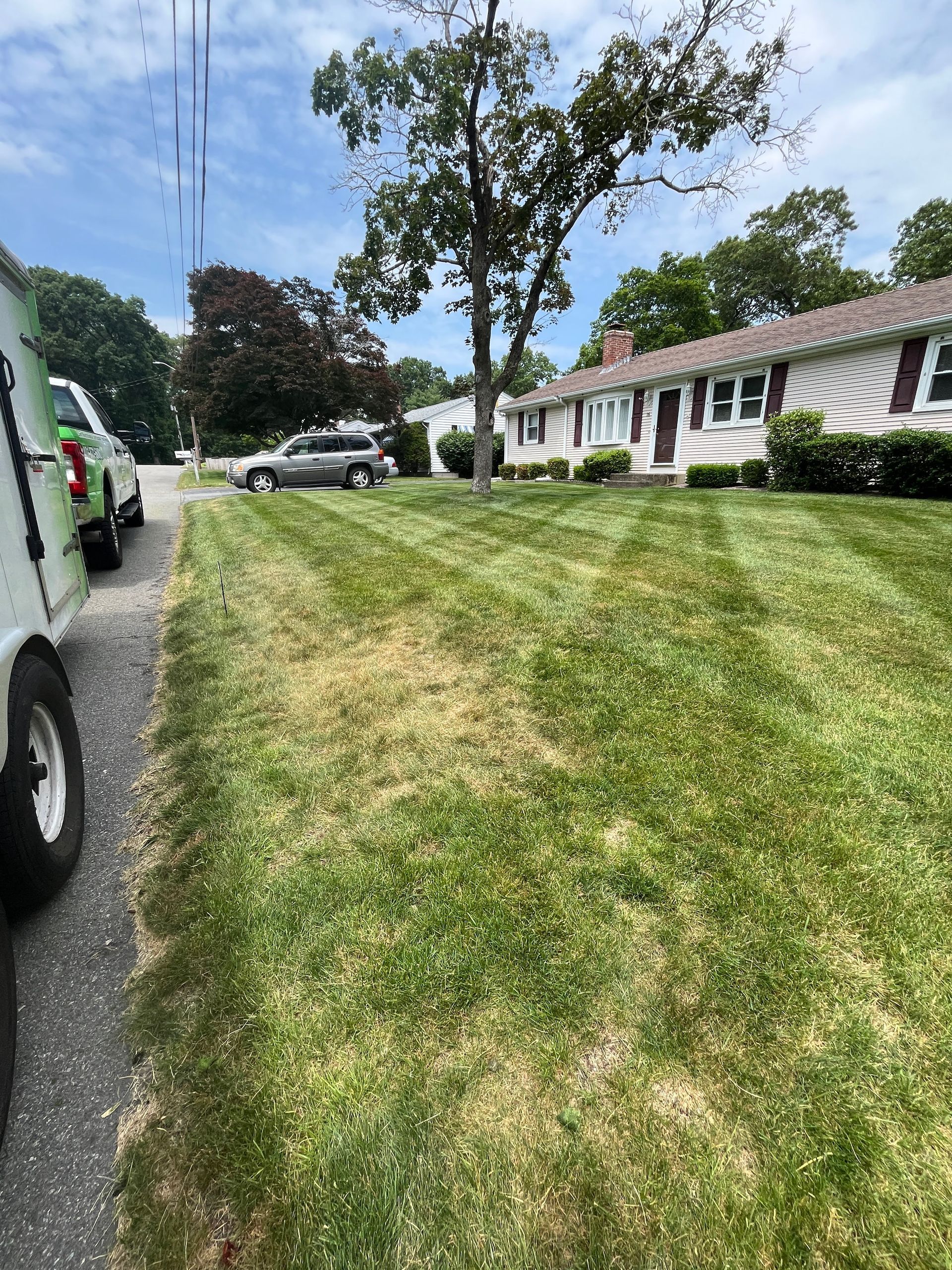 A truck is parked in front of a lush green lawn in front of a house.