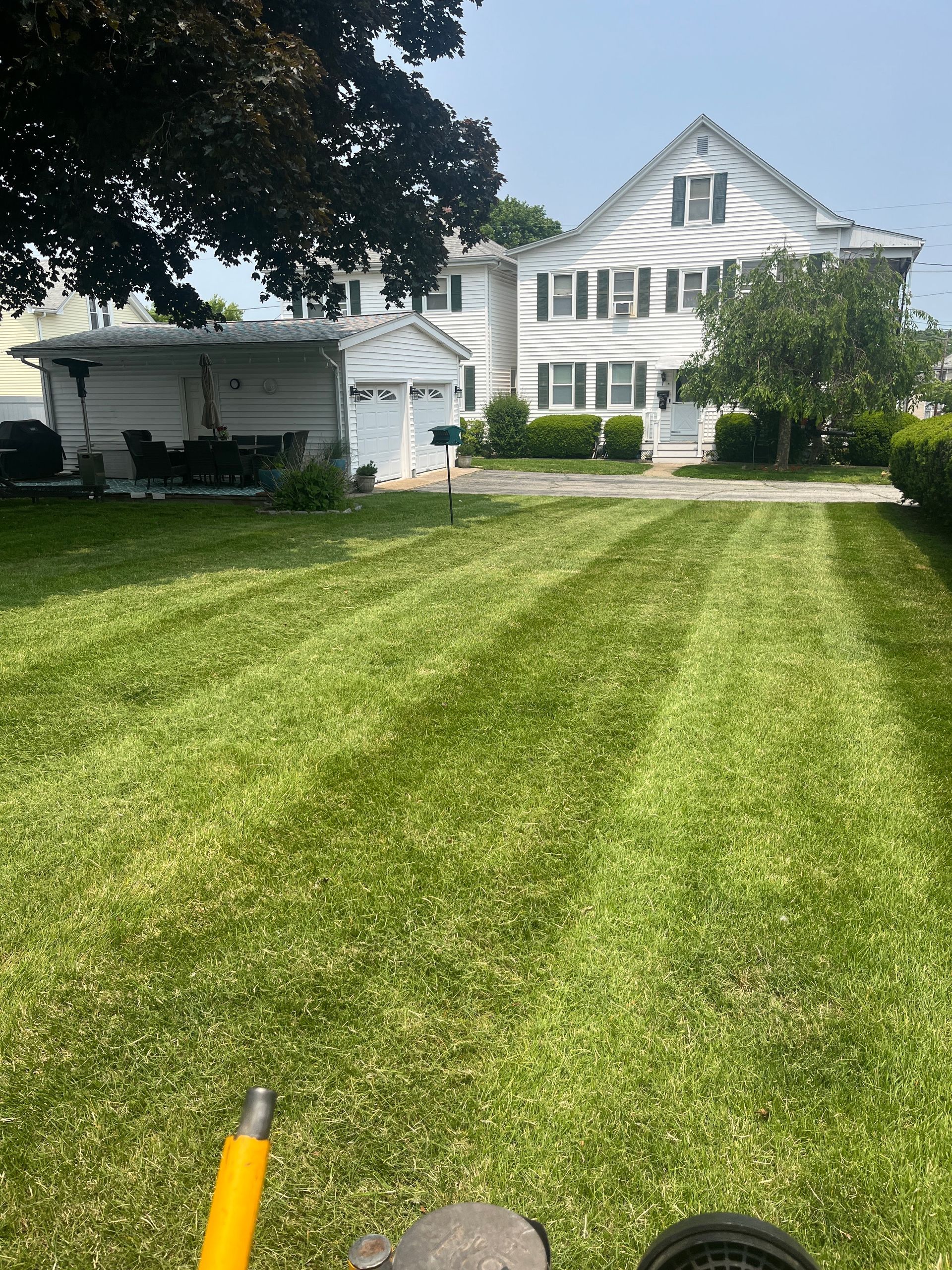A lawn mower is cutting a lush green lawn in front of a house.