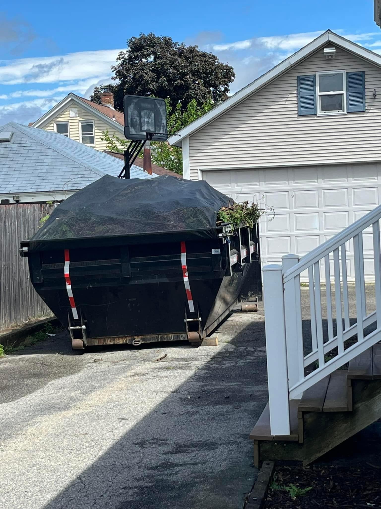 A dumpster is parked in a driveway next to a house.