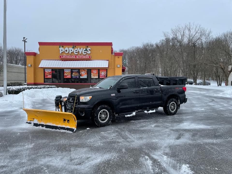A black truck with a snow plow attached to it is parked in front of a popeye 's restaurant.