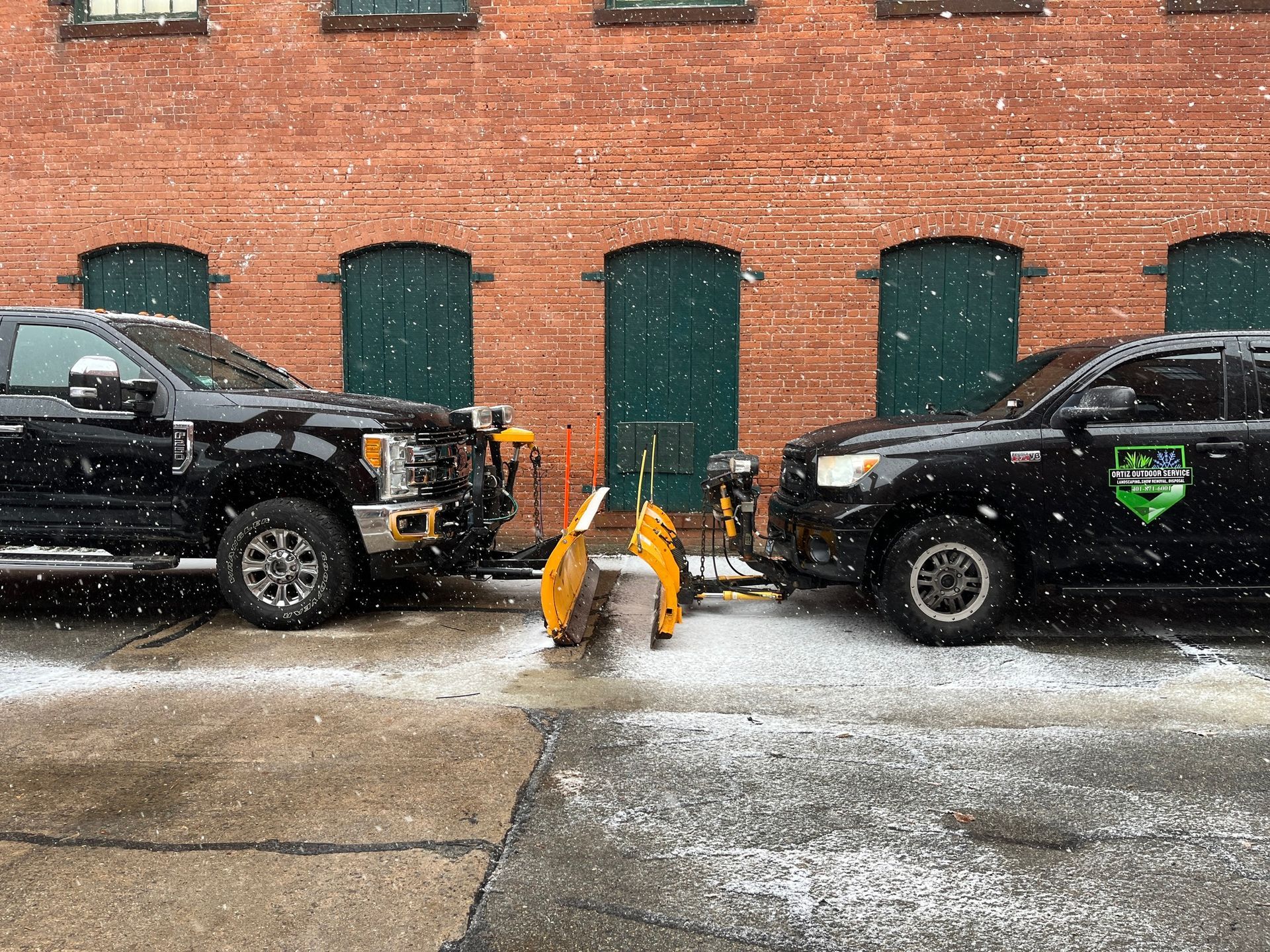 Two snow plows are parked in front of a brick building.