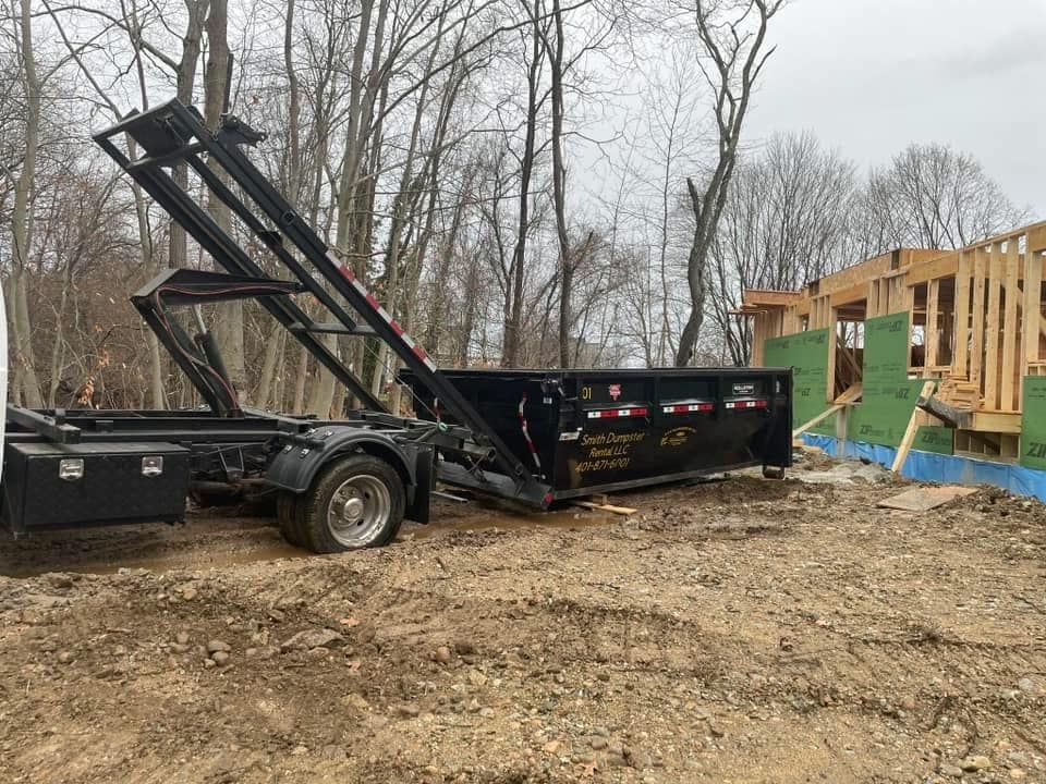 A dumpster is sitting on top of a trailer in a dirt field.