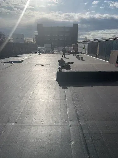Rooftop with dark paving, benches, and a bright sunlit skyline in the distance