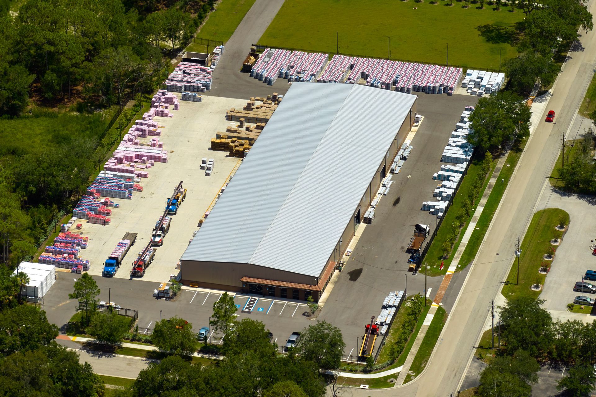 Aerial view of a large white-roofed tent at a busy outdoor event with rows of parked cars and trees nearby
