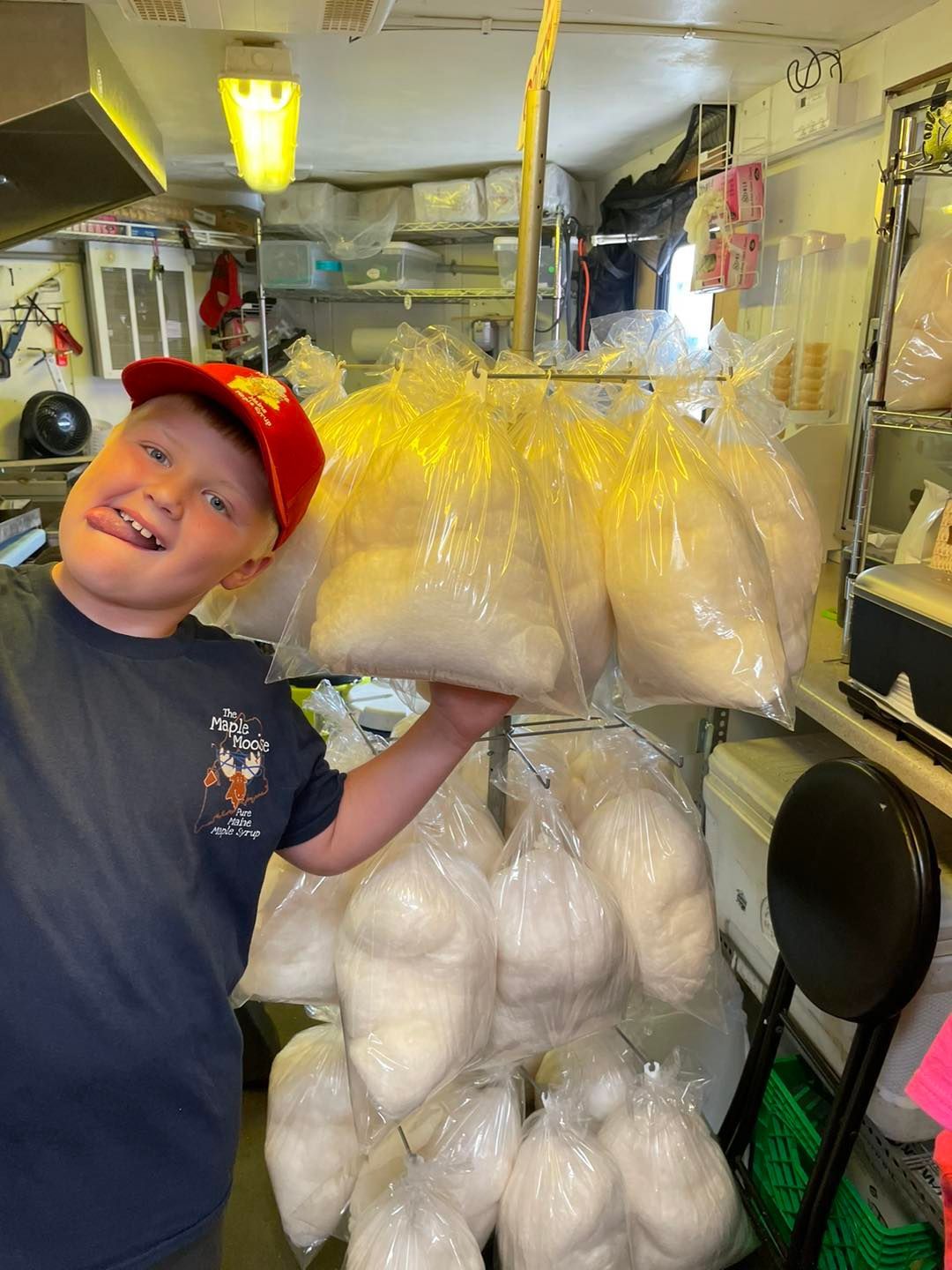Boy holding many bags of cotton candy, sticking out tongue, in a shop setting.